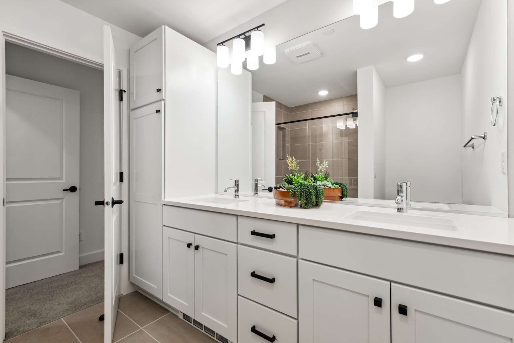 A modern and minimalist bathroom with white cabinets, a large vanity mirror, and a potted plant on the counter.
