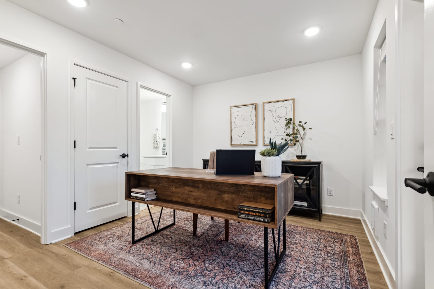 A cozy and minimalist home office space with a wooden desk, a patterned rug, and decorative elements on the walls.
