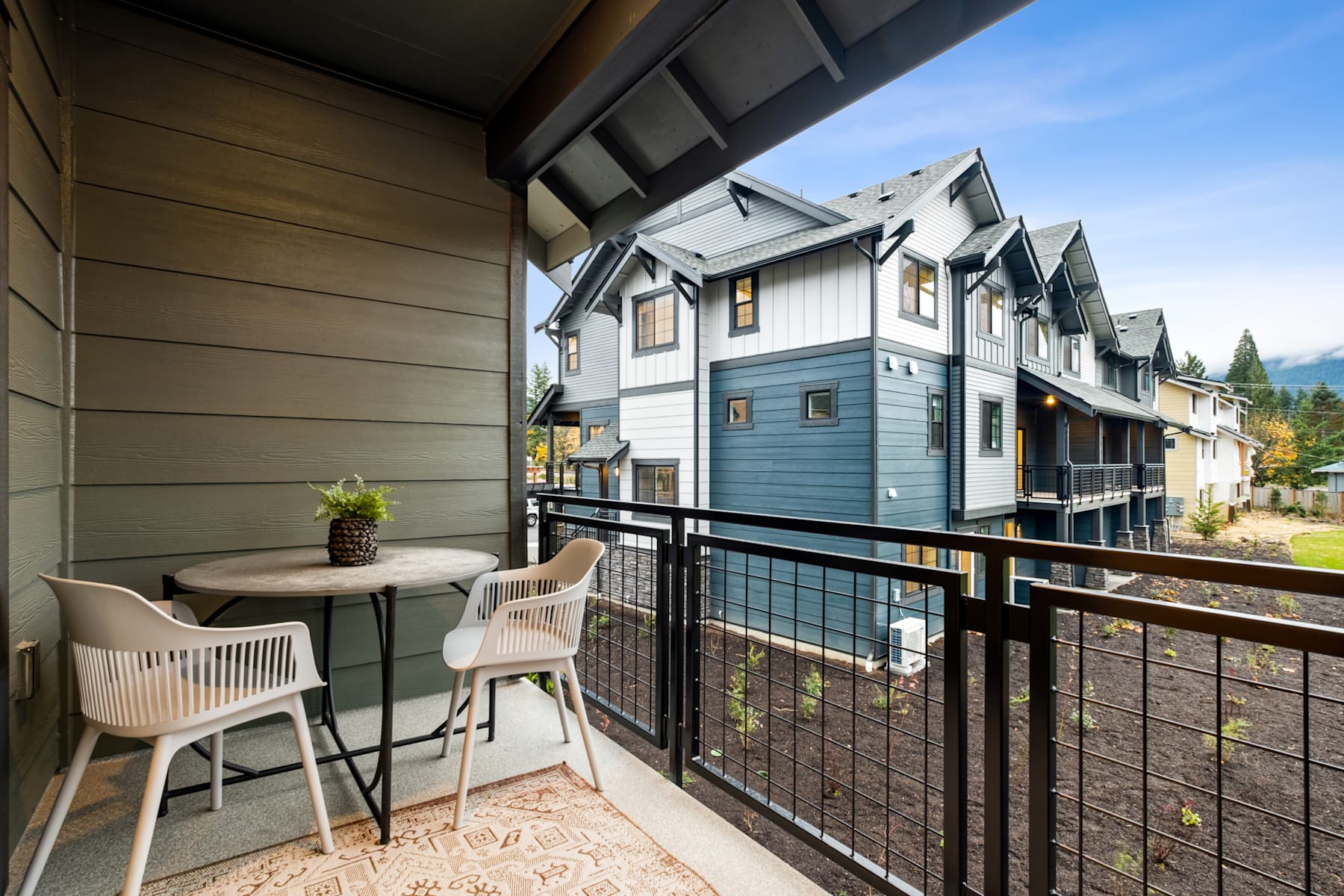 A cozy balcony with a small table and chairs overlooking a scenic neighborhood with multi-story residential buildings in the background.