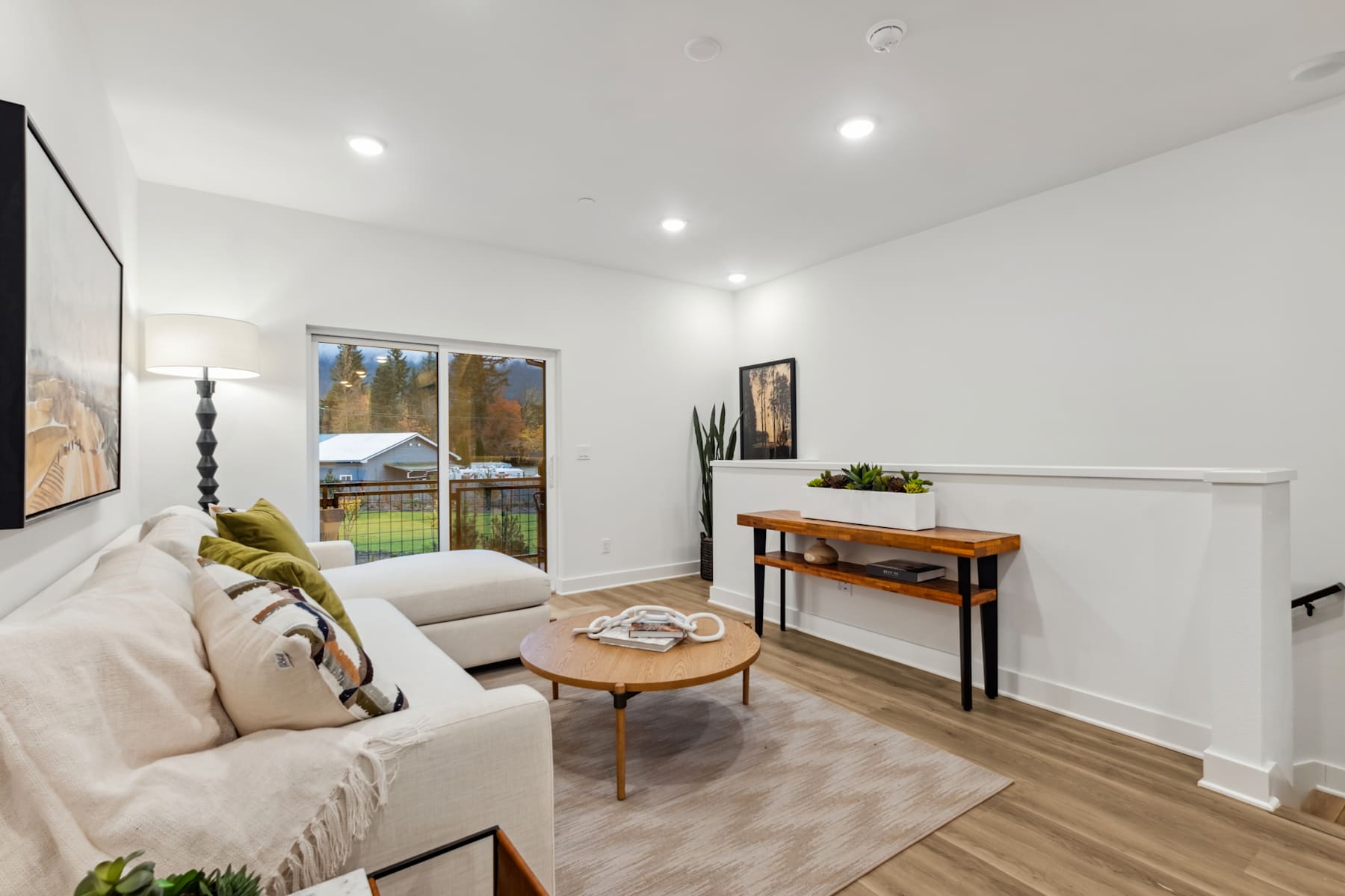 A cozy and well-furnished living room with a comfortable sofa, a wooden coffee table, and a console table with decorative items, set against a backdrop of a large window overlooking a scenic outdoor view.