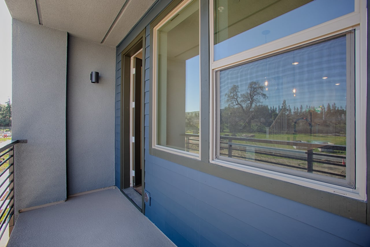 A modern hallway with large windows overlooking a scenic outdoor landscape, featuring a blue floor and a wooden railing.