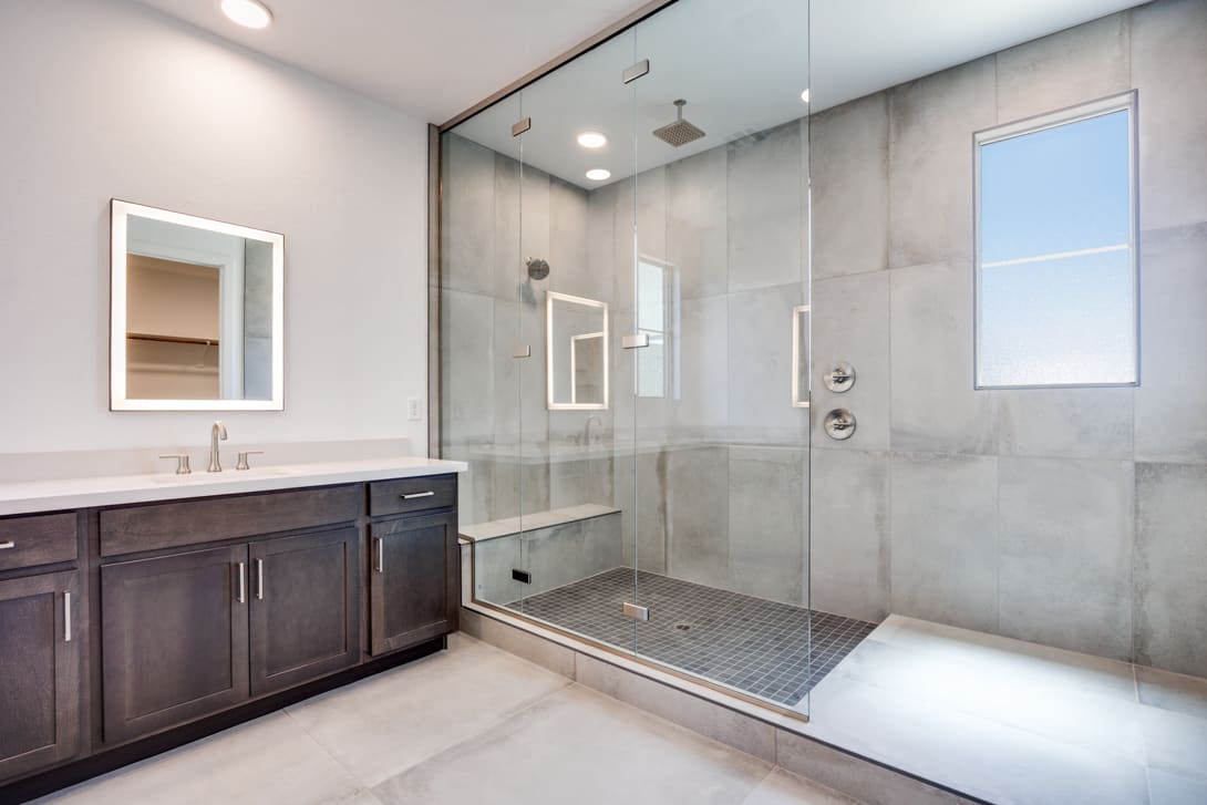 A modern bathroom with a large glass shower enclosure, a dark wood vanity, and a mirror on the wall.