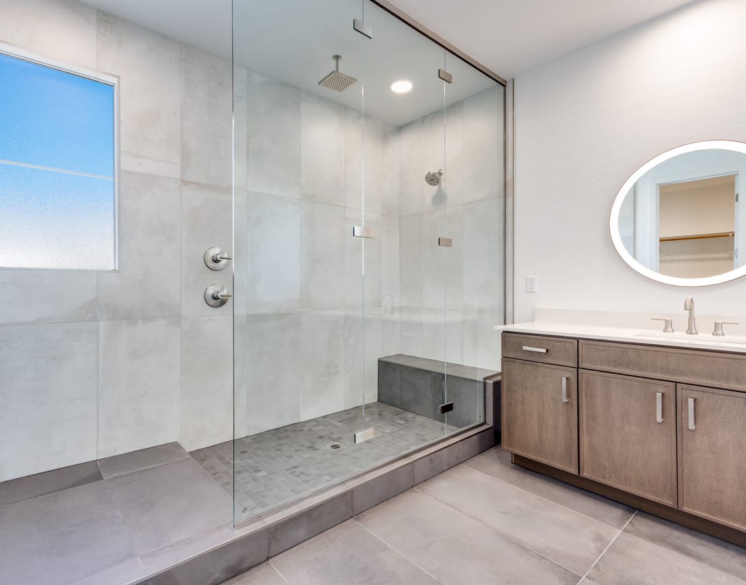 A modern, spacious bathroom with a large glass shower enclosure, a vanity with a mirror, and a window providing natural light.