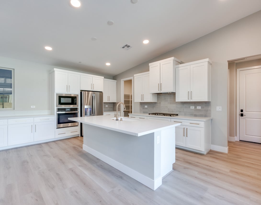 A modern, bright kitchen with white cabinets, a large island, and stainless steel appliances, set against a backdrop of hardwood floors and neutral-colored walls.