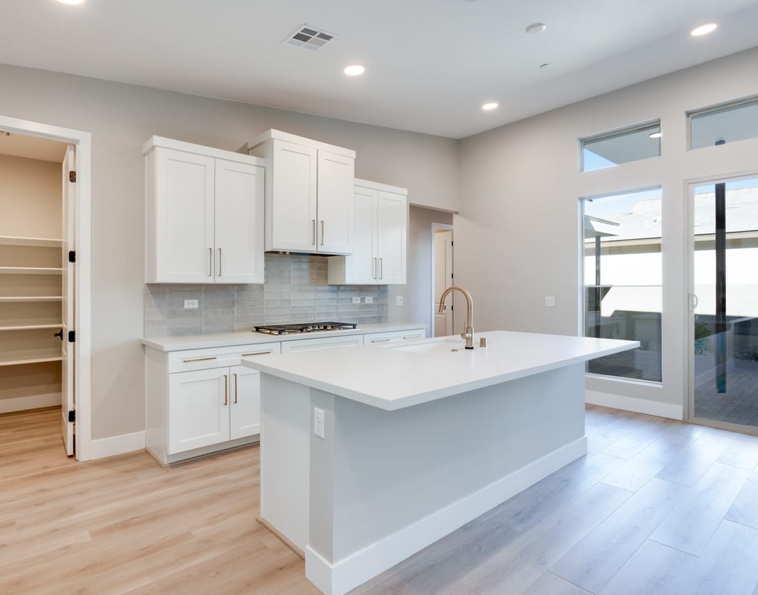 A modern, open-concept kitchen with white cabinets, a large island, and hardwood floors, surrounded by large windows that let in natural light.