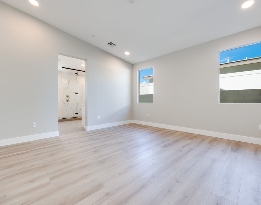 A spacious, well-lit room with a hardwood floor, a door leading to another area, and large windows providing natural light.