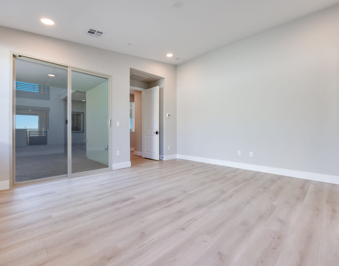 A spacious, well-lit room with a smooth, light-colored wooden floor, a sliding glass door, and a closet door visible in the background.