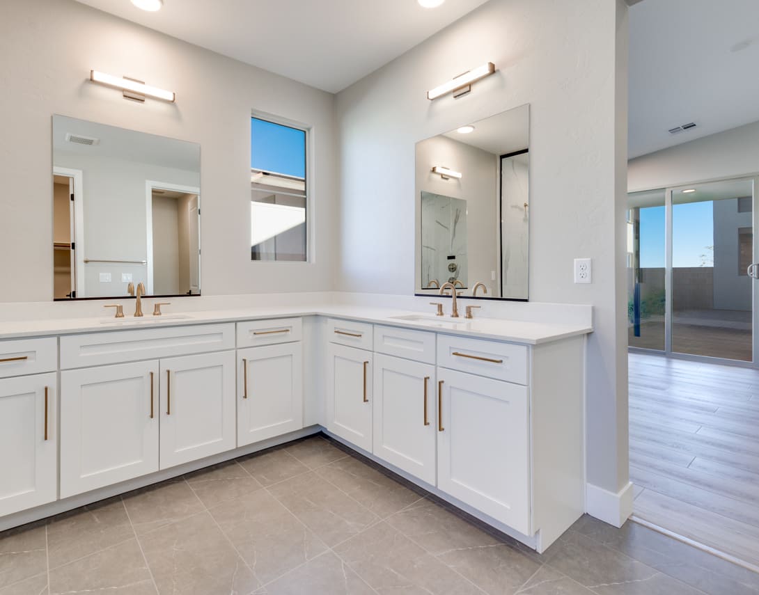A spacious and modern bathroom with white cabinets, a double vanity, and large mirrors, set against a backdrop of natural light and a view of the outdoors.