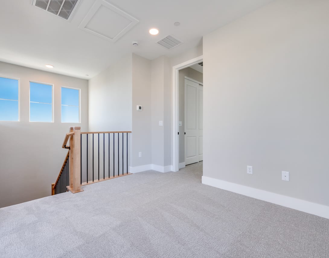 A bright, spacious room with a carpeted floor, a metal railing, and a doorway leading to another area.