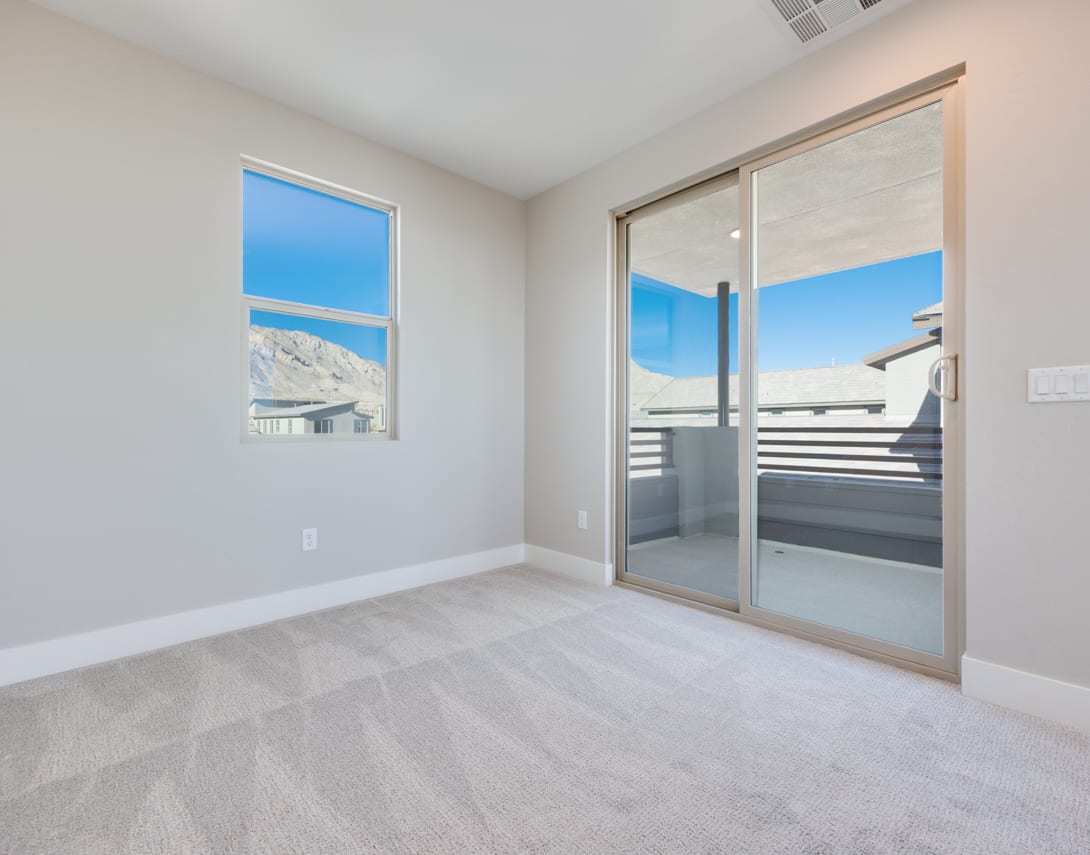 A bright and spacious room with large windows offering a scenic view of the snowy mountains in the background, and a sliding glass door leading to a balcony or patio in the foreground.
