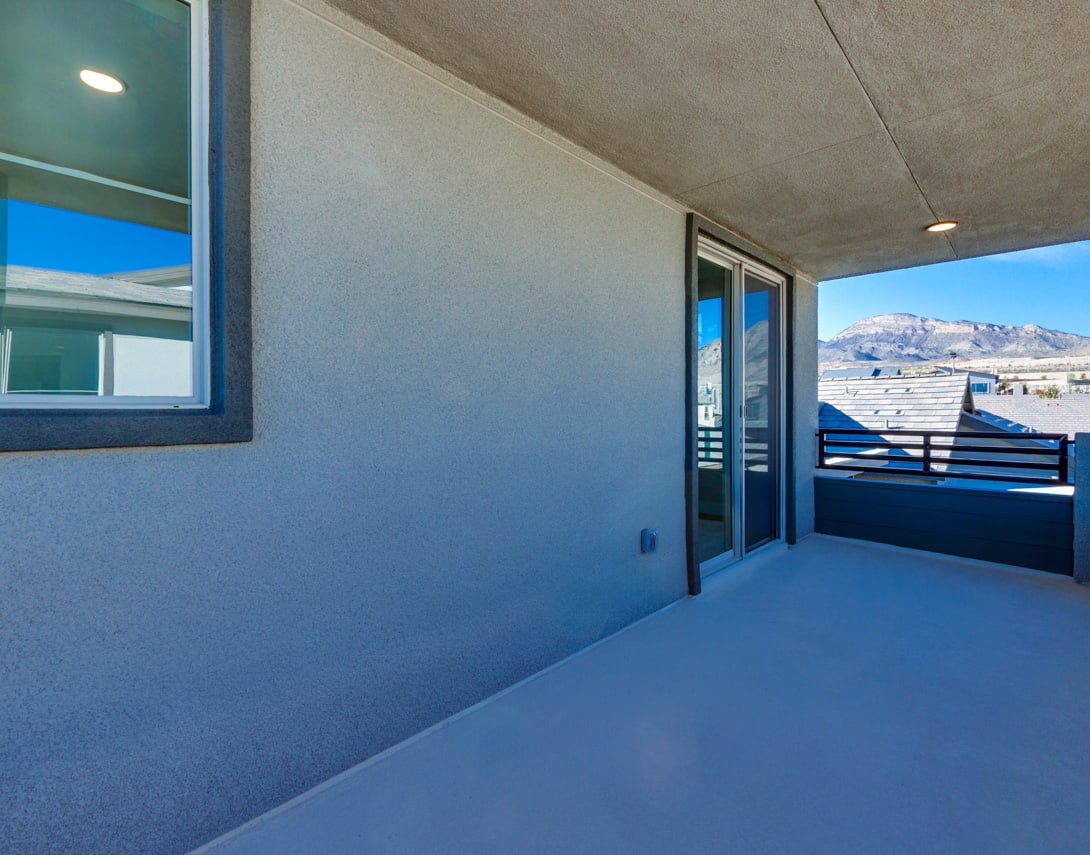 A modern, minimalist balcony with a concrete floor, glass sliding doors, and a scenic mountain view in the background.