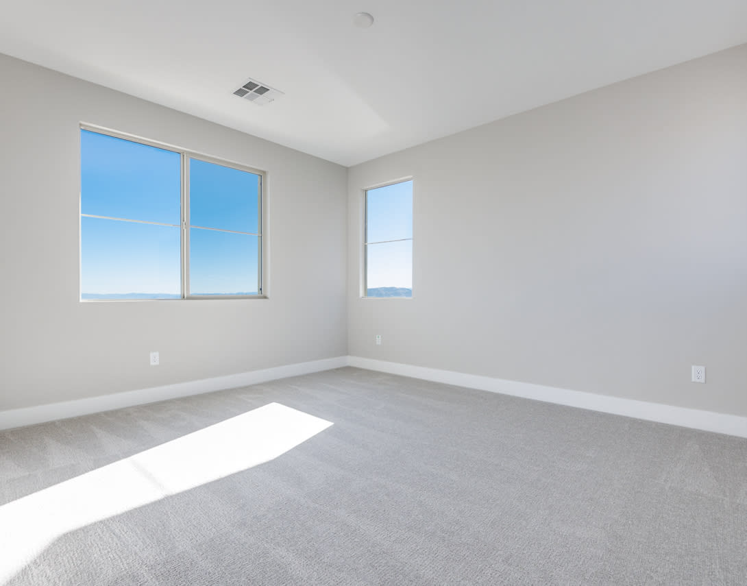 An empty, bright room with large windows overlooking a clear sky.