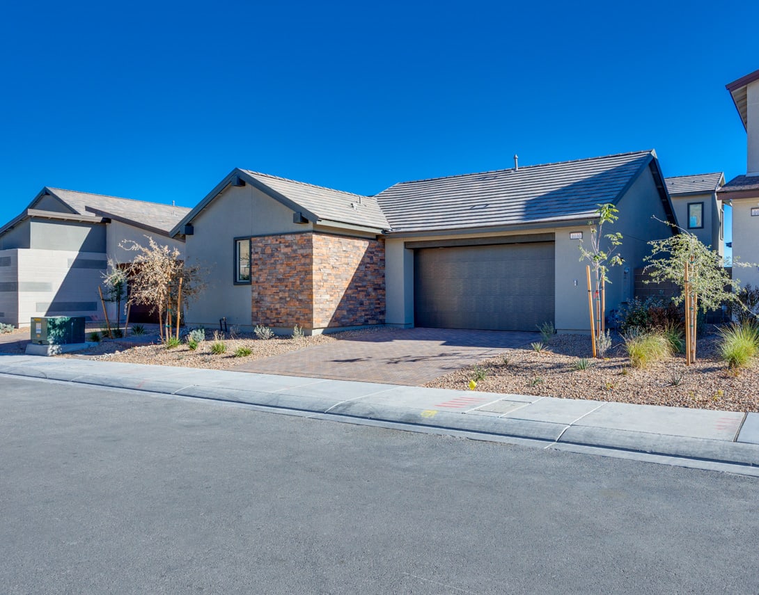 A modern, single-story residential home with a garage, surrounded by landscaping and situated against a clear blue sky.
