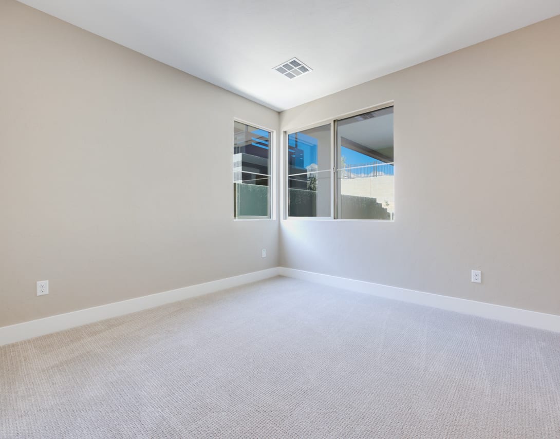 An empty room with white walls, a carpeted floor, and a window providing natural light.