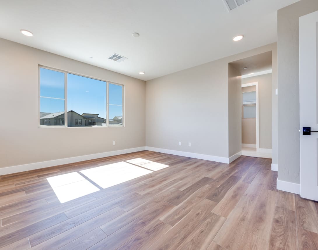 A spacious, well-lit room with hardwood floors, neutral-colored walls, and large windows providing a view of the exterior.