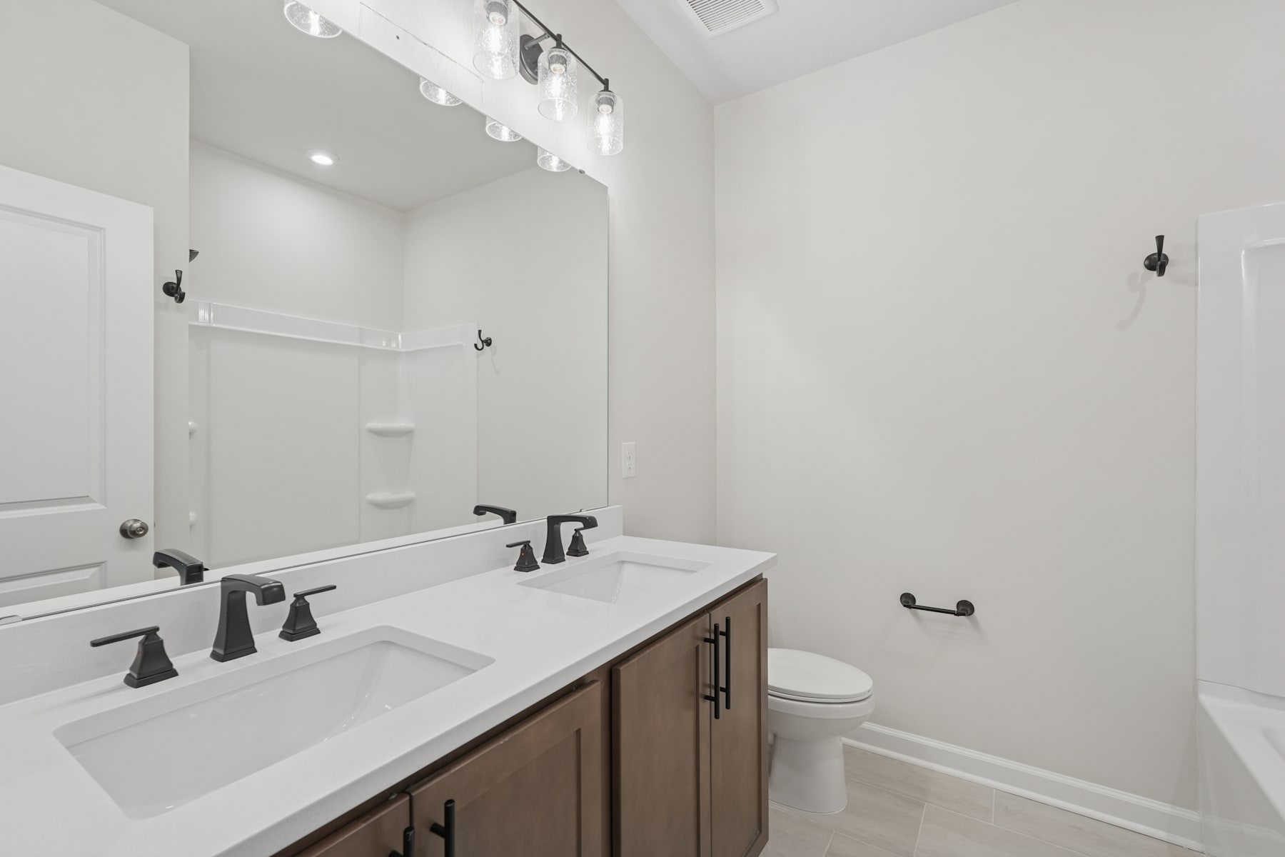 A modern, minimalist bathroom with a double vanity, white countertop, and black fixtures, set against a bright, airy background.