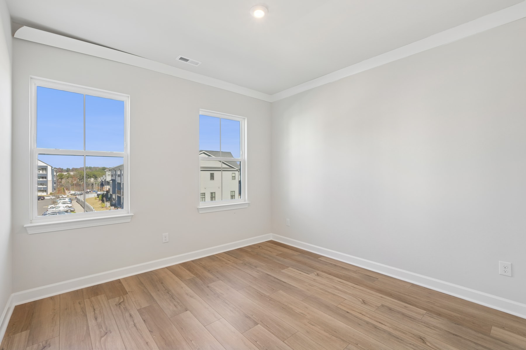 A bright and spacious room with large windows overlooking a residential neighborhood, featuring hardwood floors and a clean, minimalist design.