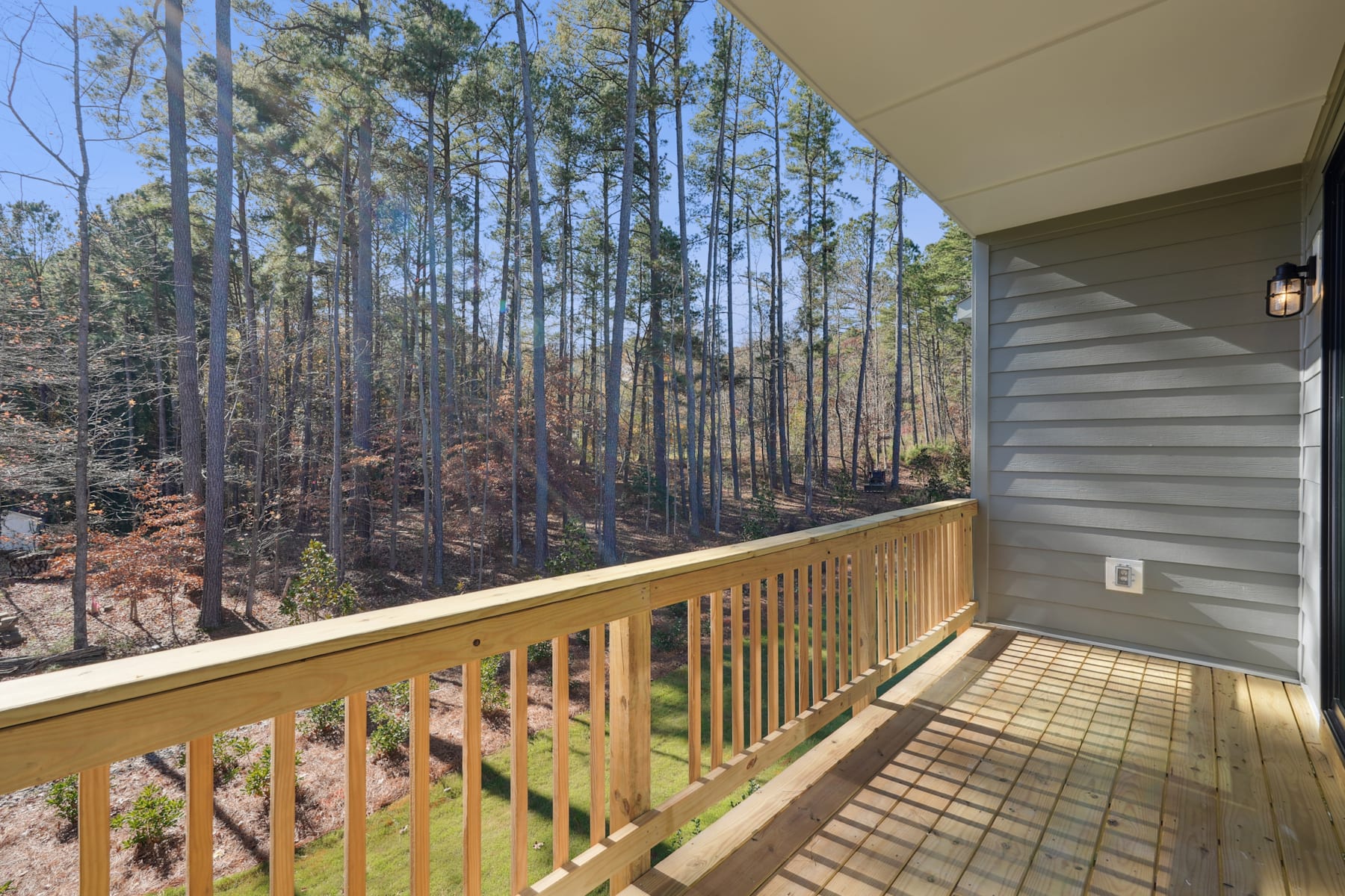 A wooden deck with a railing overlooks a forest of tall pine trees in the background.