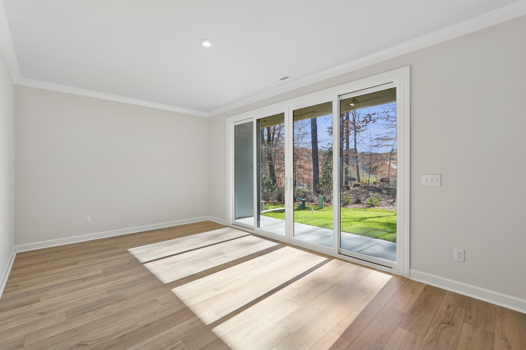 A bright and spacious room with large sliding glass doors that open onto a lush, green backyard landscape.