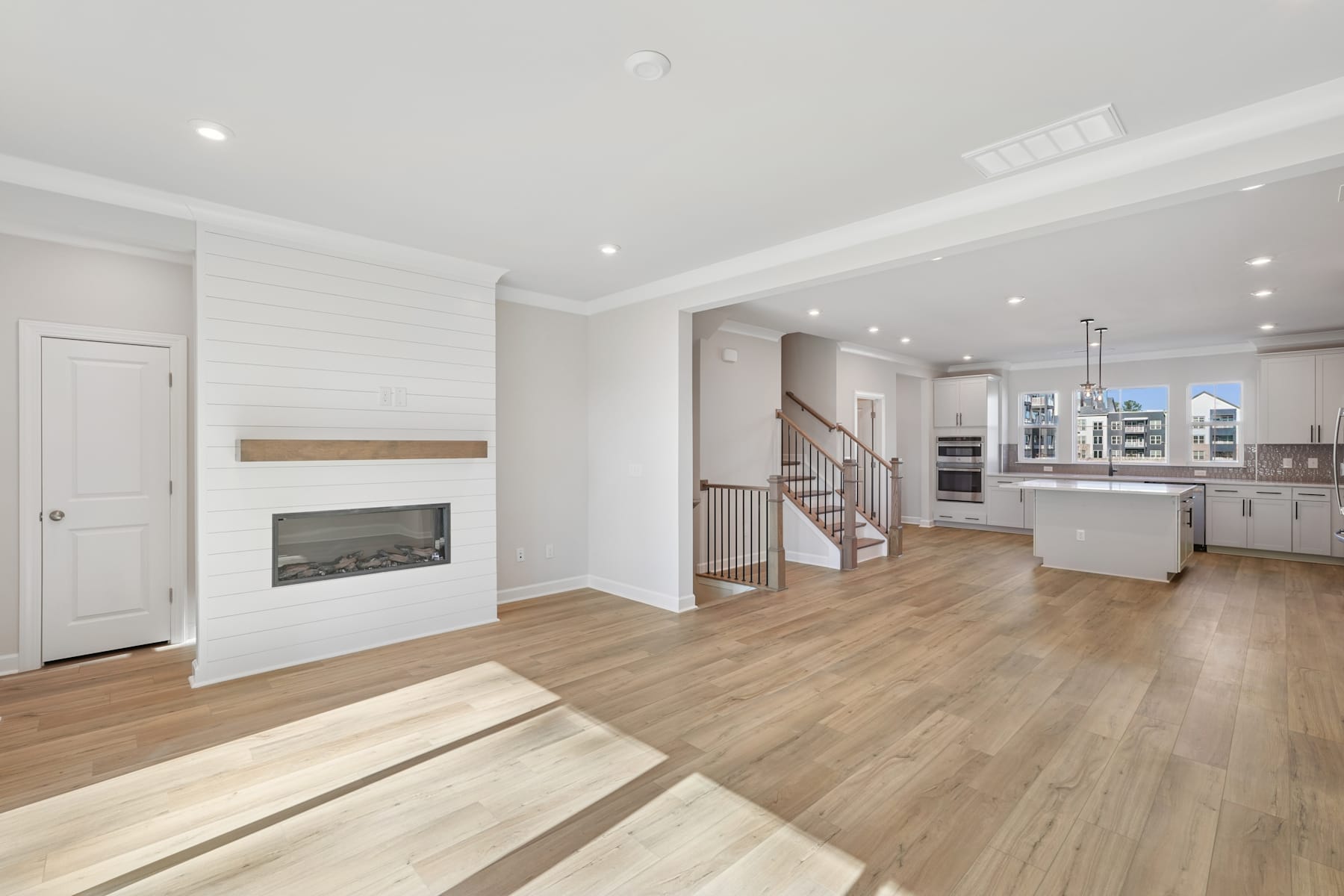 A spacious and modern living room with a fireplace, hardwood floors, and an open-concept kitchen visible in the background.