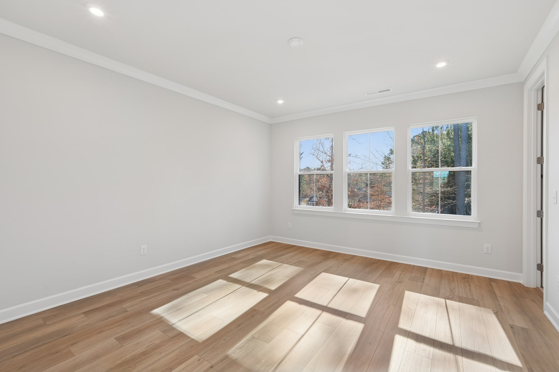 An empty room with white walls, hardwood floors, and large windows allowing natural light to stream in, creating a bright and airy atmosphere.