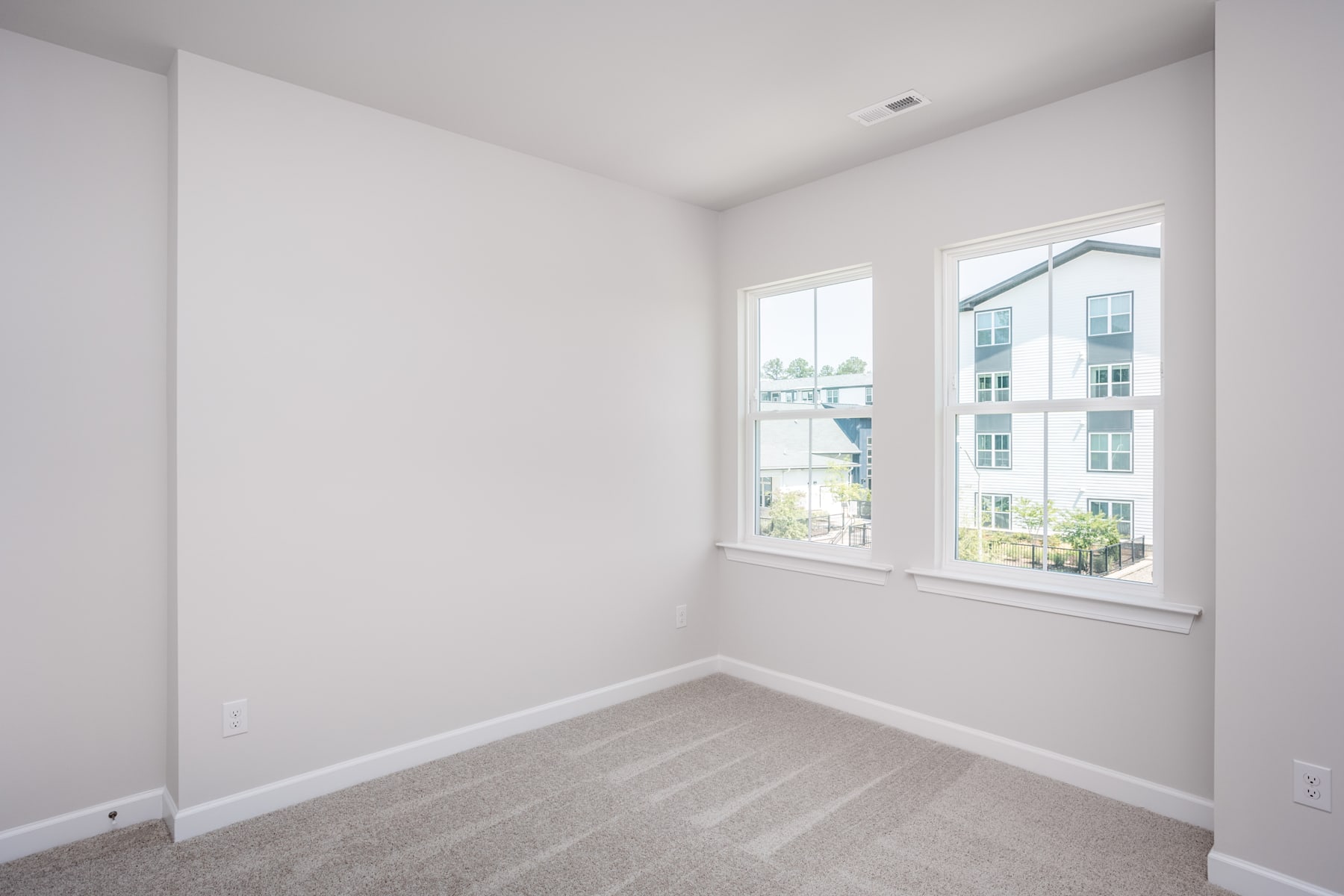A bright, empty room with white walls, a large window, and a hardwood floor.