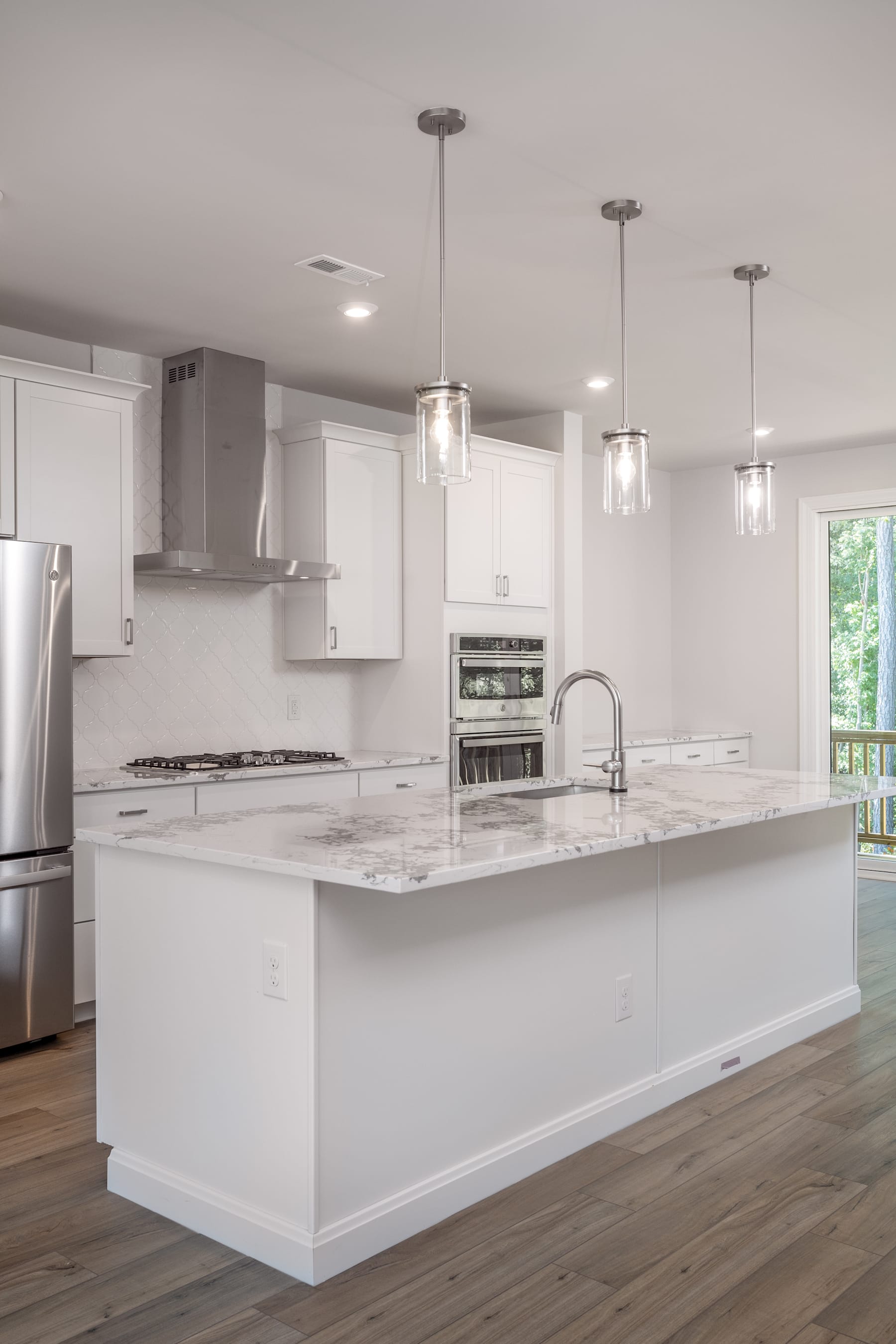 A modern, bright, and spacious kitchen with white cabinets, marble countertops, and pendant lighting fixtures.