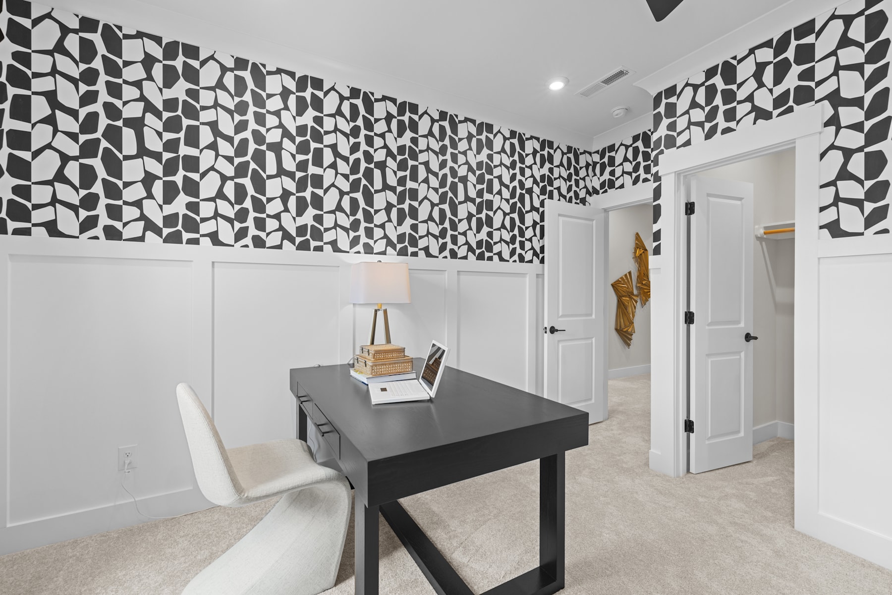 A modern, minimalist office space with a black and white geometric patterned wall, a simple black desk, and a white chair.