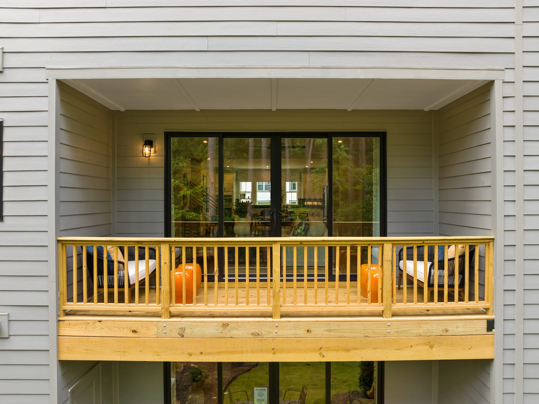 A wooden porch with a railing overlooks a lush, green outdoor area surrounded by a white siding house.