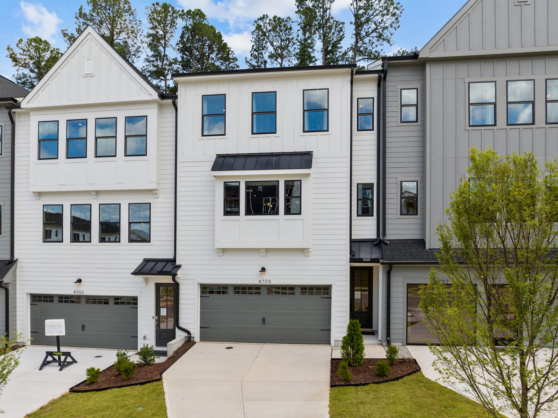 A modern, multi-story townhouse with a garage, surrounded by trees and greenery in the foreground.
