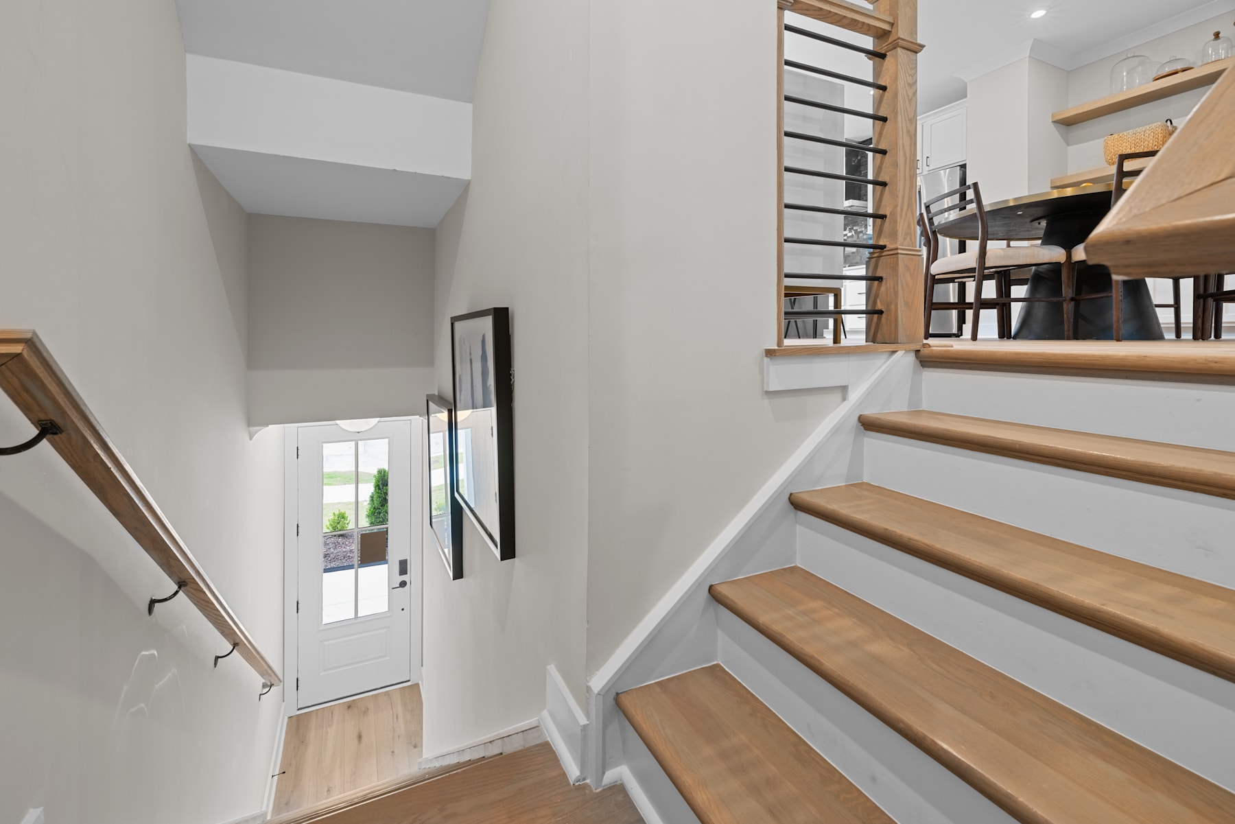 A modern, minimalist staircase with wooden steps and a white wall backdrop, leading to a doorway with a view of the outdoors.