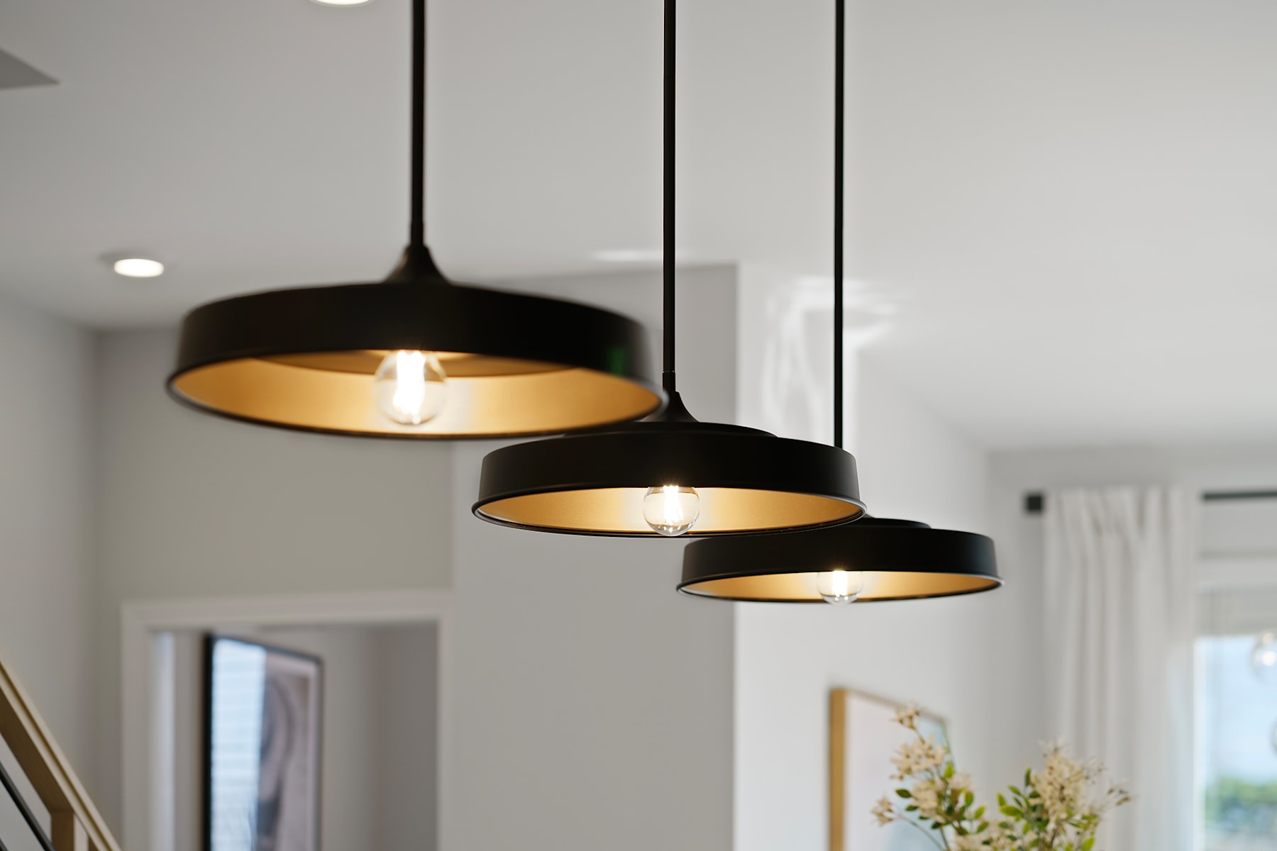 Three black pendant lamps with golden interiors hang from the ceiling in a bright, minimalist room.