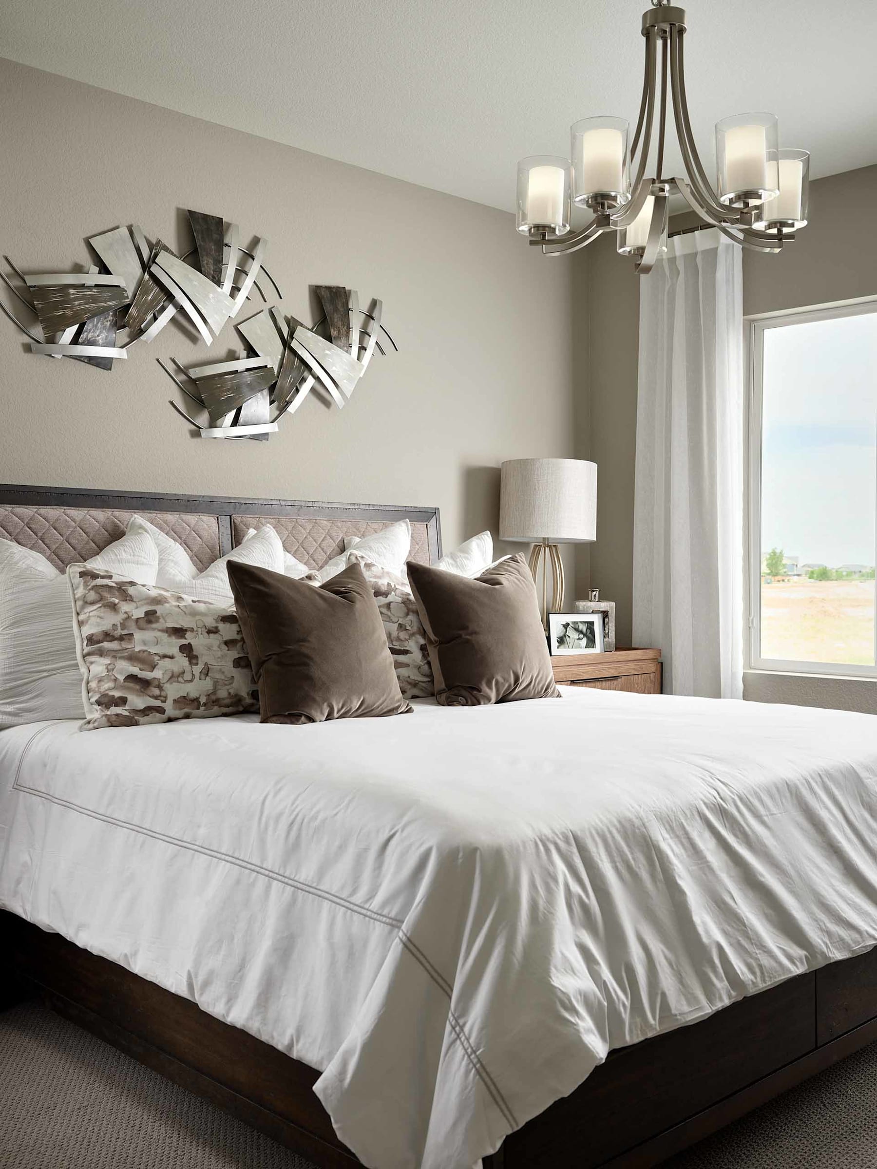 A modern and cozy bedroom with a large bed, plush bedding, and a decorative light fixture on the ceiling. The walls feature an abstract art piece, adding a touch of visual interest to the space.