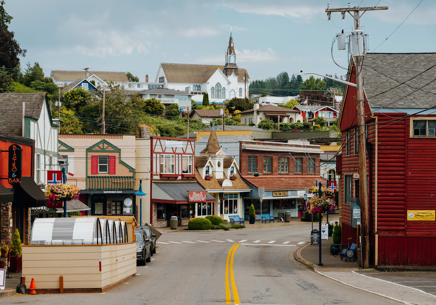 A colorful and quaint town nestled in a hilly landscape, with a mix of traditional and modern buildings, shops, and a church steeple visible in the background.