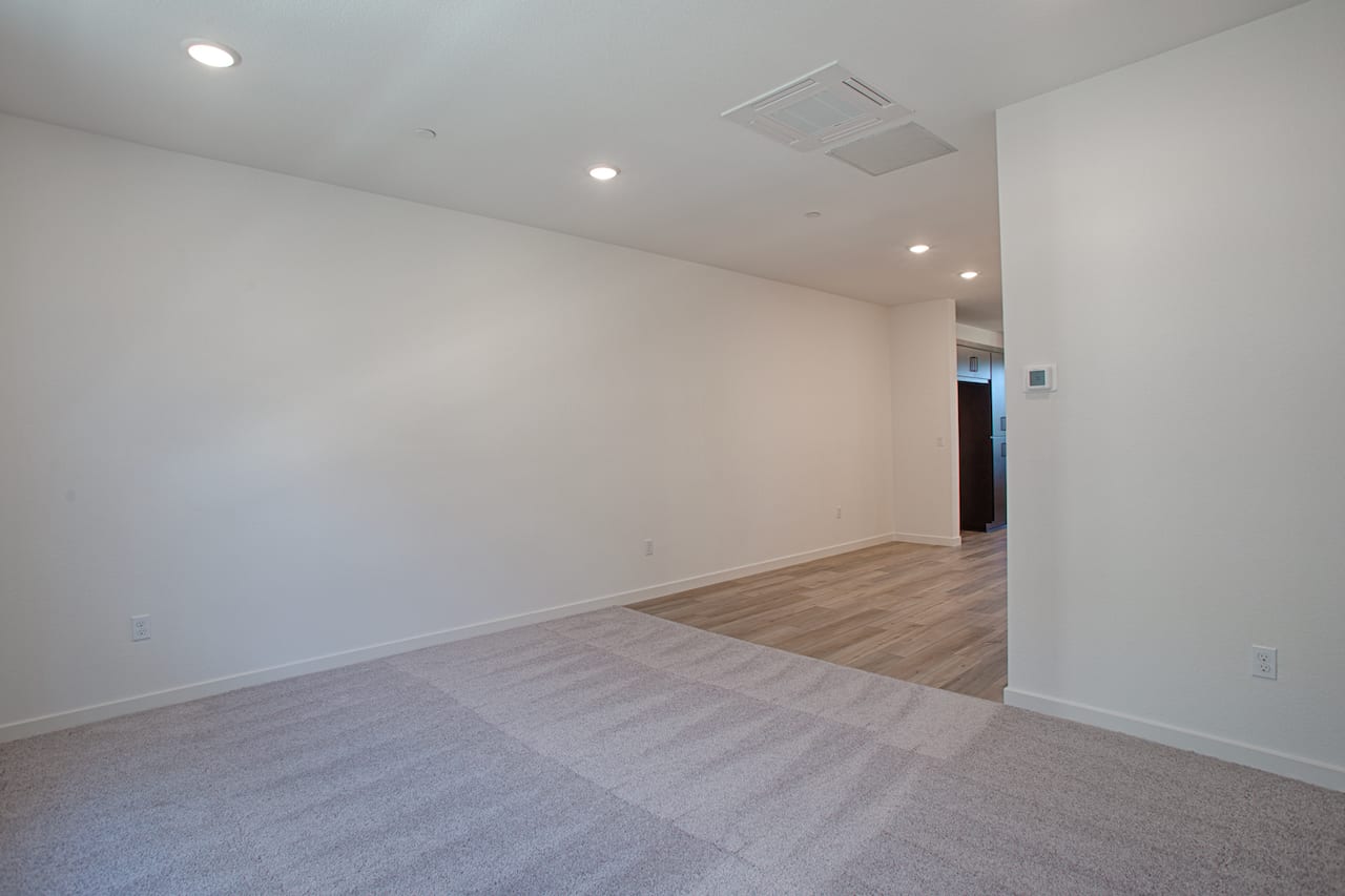 An empty, well-lit room with white walls, a hardwood floor, and recessed lighting fixtures in the ceiling.