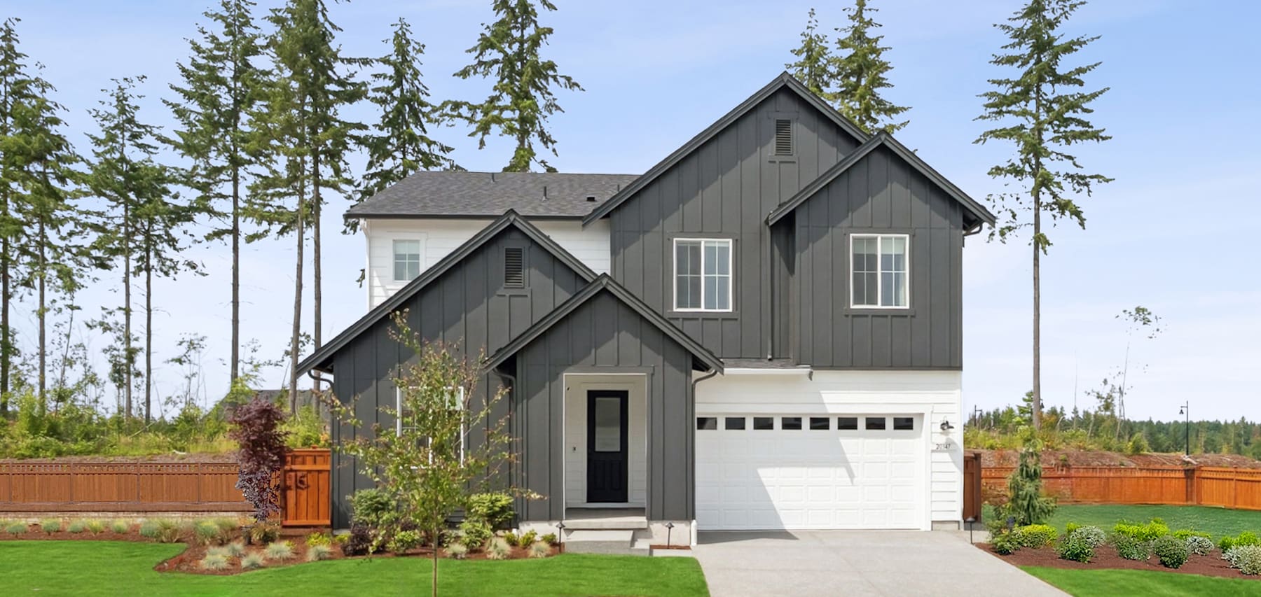 A modern, two-story house with a gray exterior and a white trim, surrounded by lush greenery and a well-manicured lawn in the foreground.