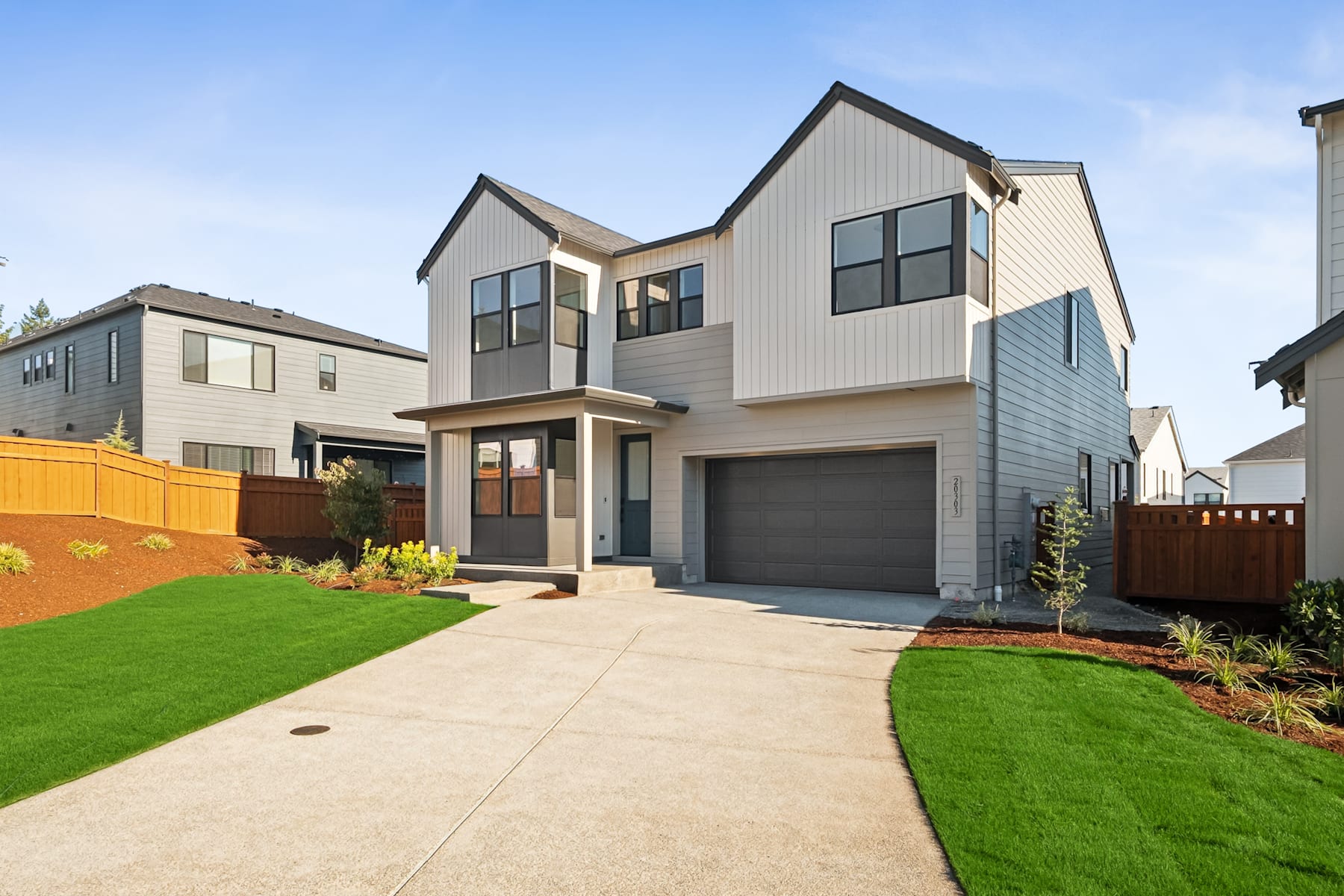 A modern two-story house with a garage, surrounded by a well-manicured lawn and landscaping, set against a clear blue sky.
