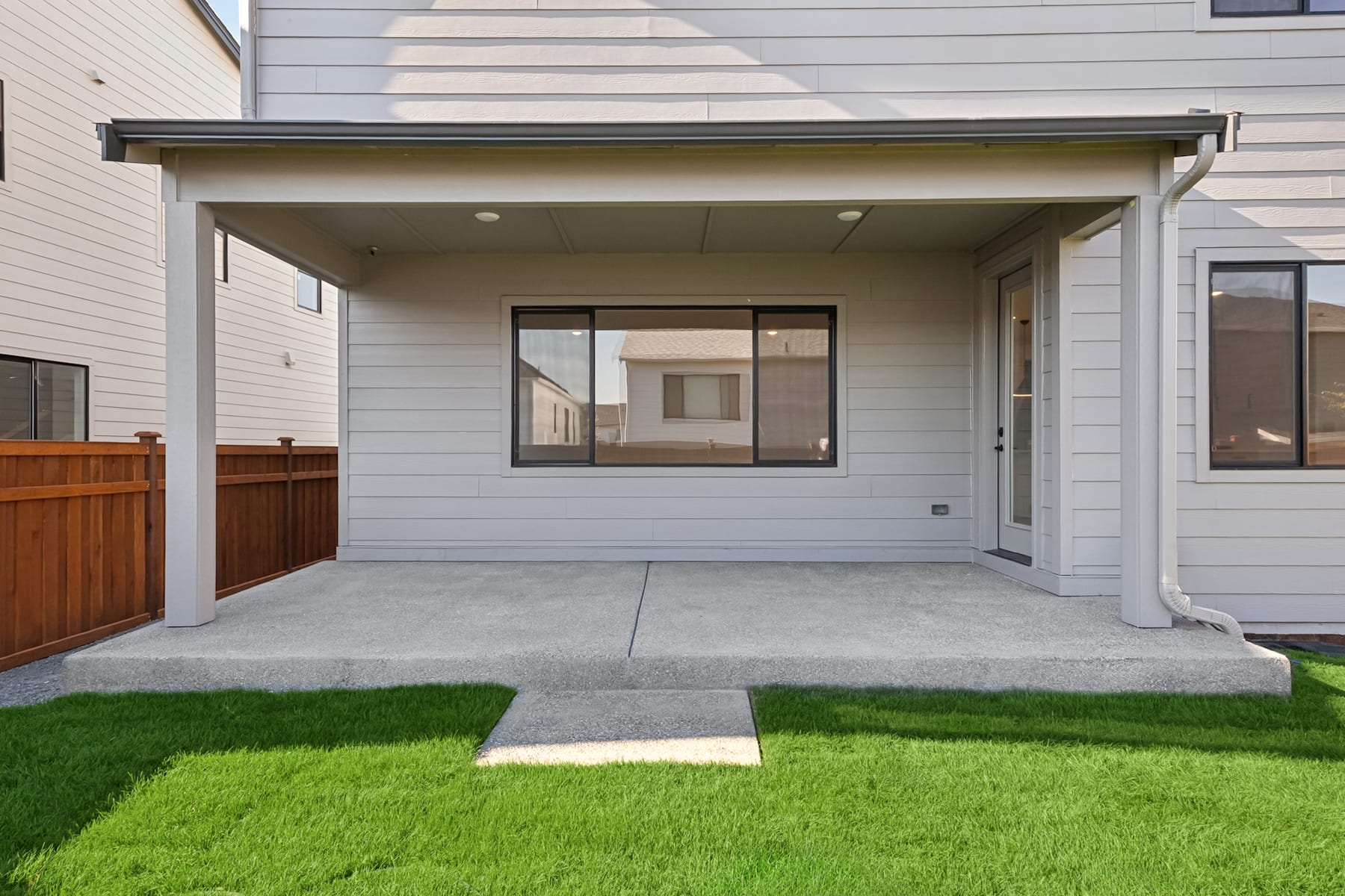 A modern, two-story residential building with a covered porch, surrounded by a well-manicured lawn and wooden fencing.