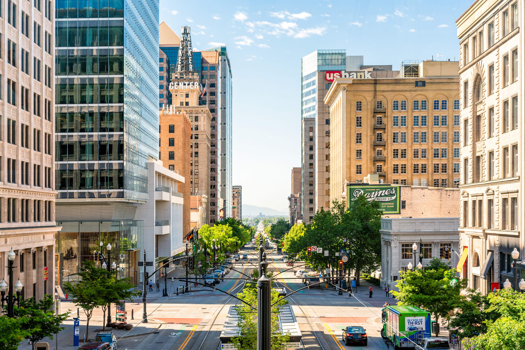 A bustling urban landscape with a mix of modern and historic buildings, lush greenery, and a busy street scene in the foreground.