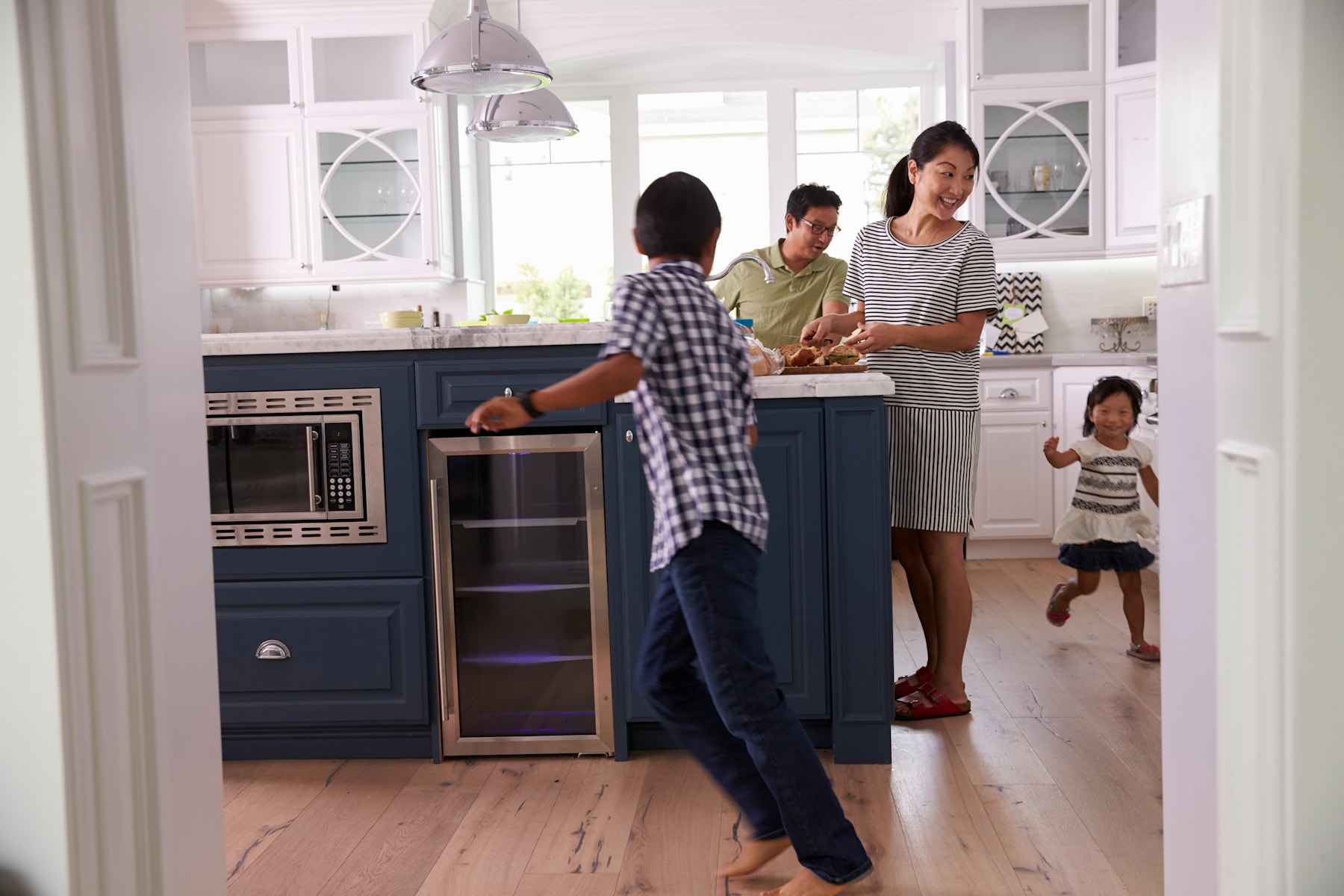 A family of four, including a woman, a man, and two children, are gathered in a bright, modern kitchen, with a kitchen island and appliances visible in the background.