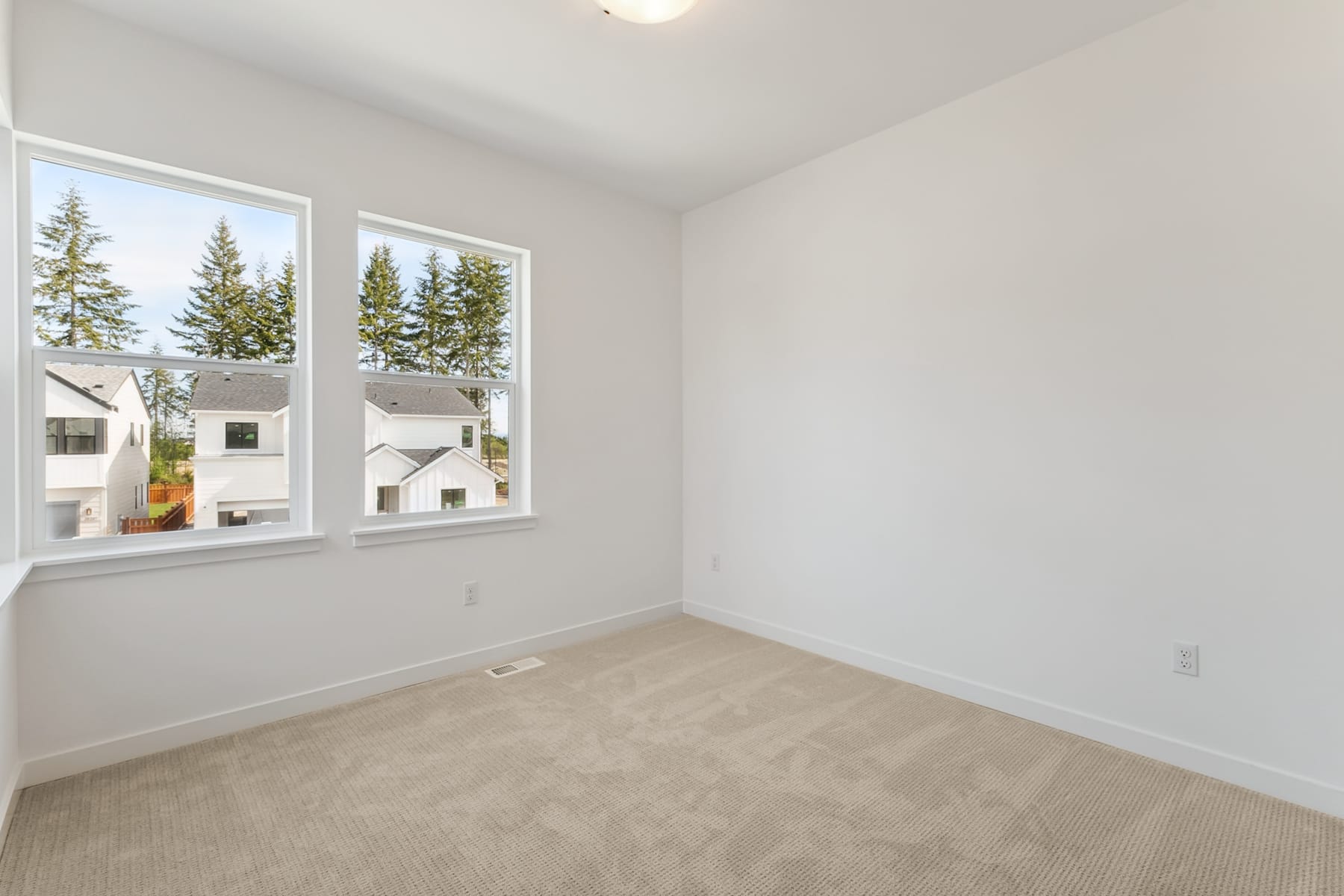 A bright and spacious room with large windows overlooking a wooded area, featuring a neutral-toned carpet and walls.