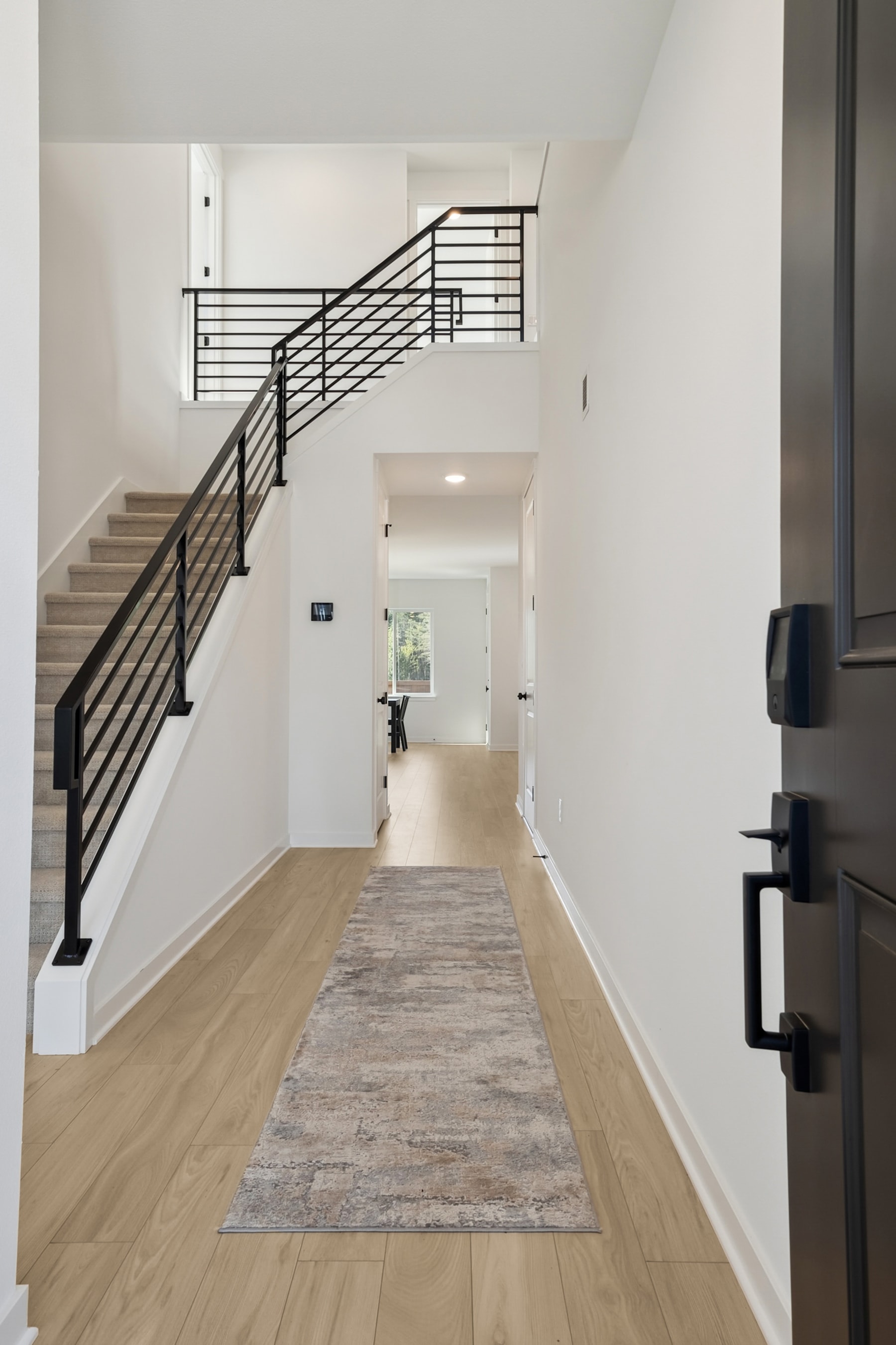 A spacious and modern hallway with a wooden floor, a decorative rug, and a staircase with black metal railings leading to an upper level.