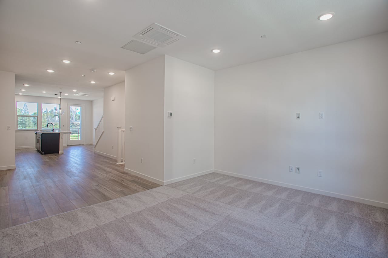 A spacious, well-lit room with a hardwood floor, recessed lighting, and a doorway leading to another area.
