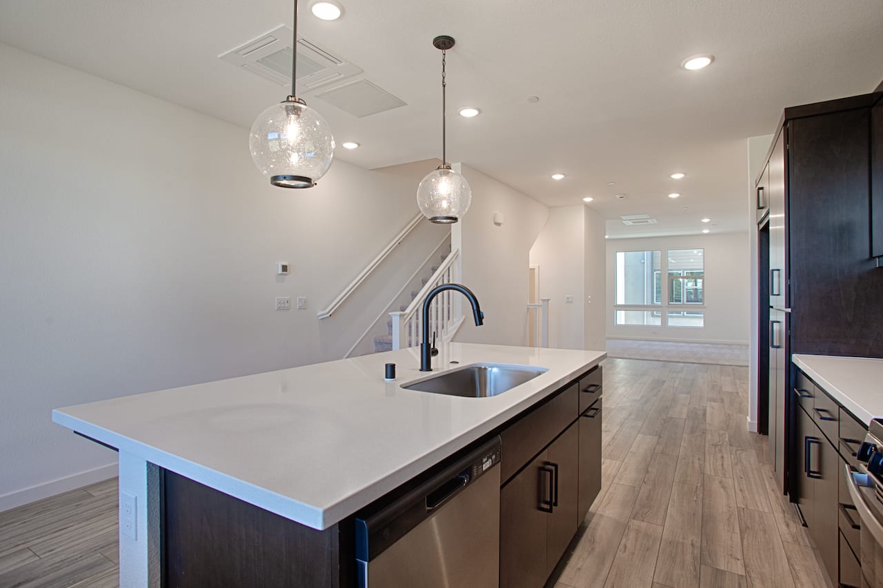 A modern, open-concept kitchen with a sleek, white countertop, stainless steel appliances, and pendant lighting fixtures that create a warm and inviting atmosphere.