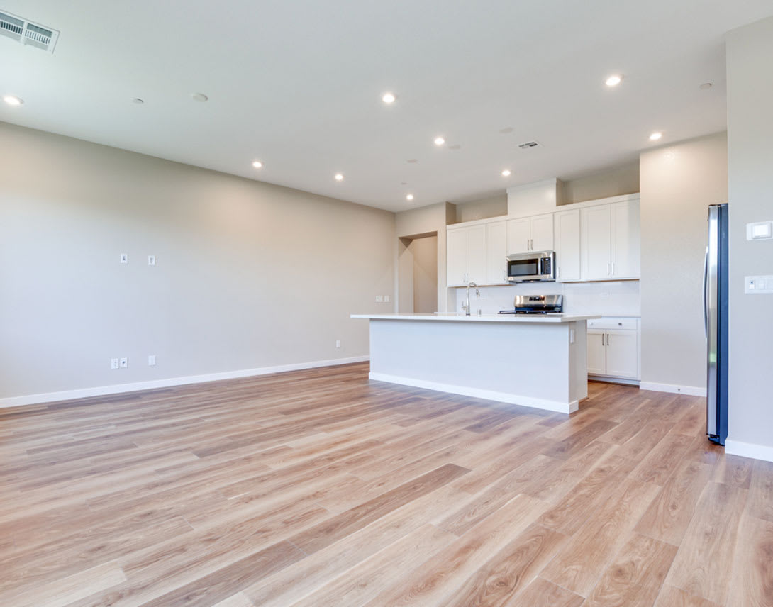A modern, open-concept kitchen and living space with white cabinets, hardwood floors, and recessed lighting.