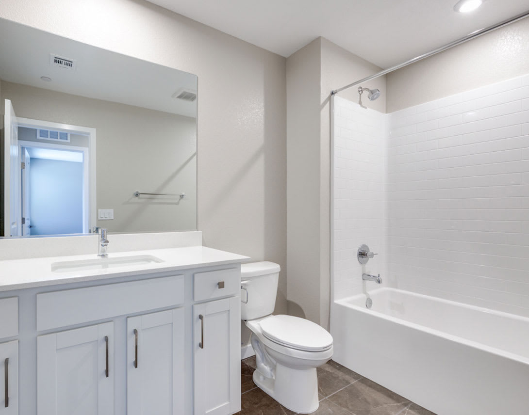A modern, well-lit bathroom with a vanity, sink, and toilet, as well as a bathtub and shower enclosure.