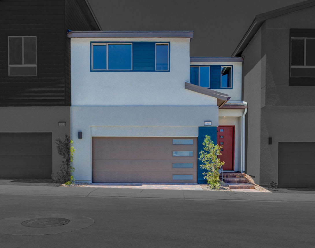 A modern, two-story residential building with a garage door, blue-tinted windows, and a small tree in the foreground, set against a dark background.
