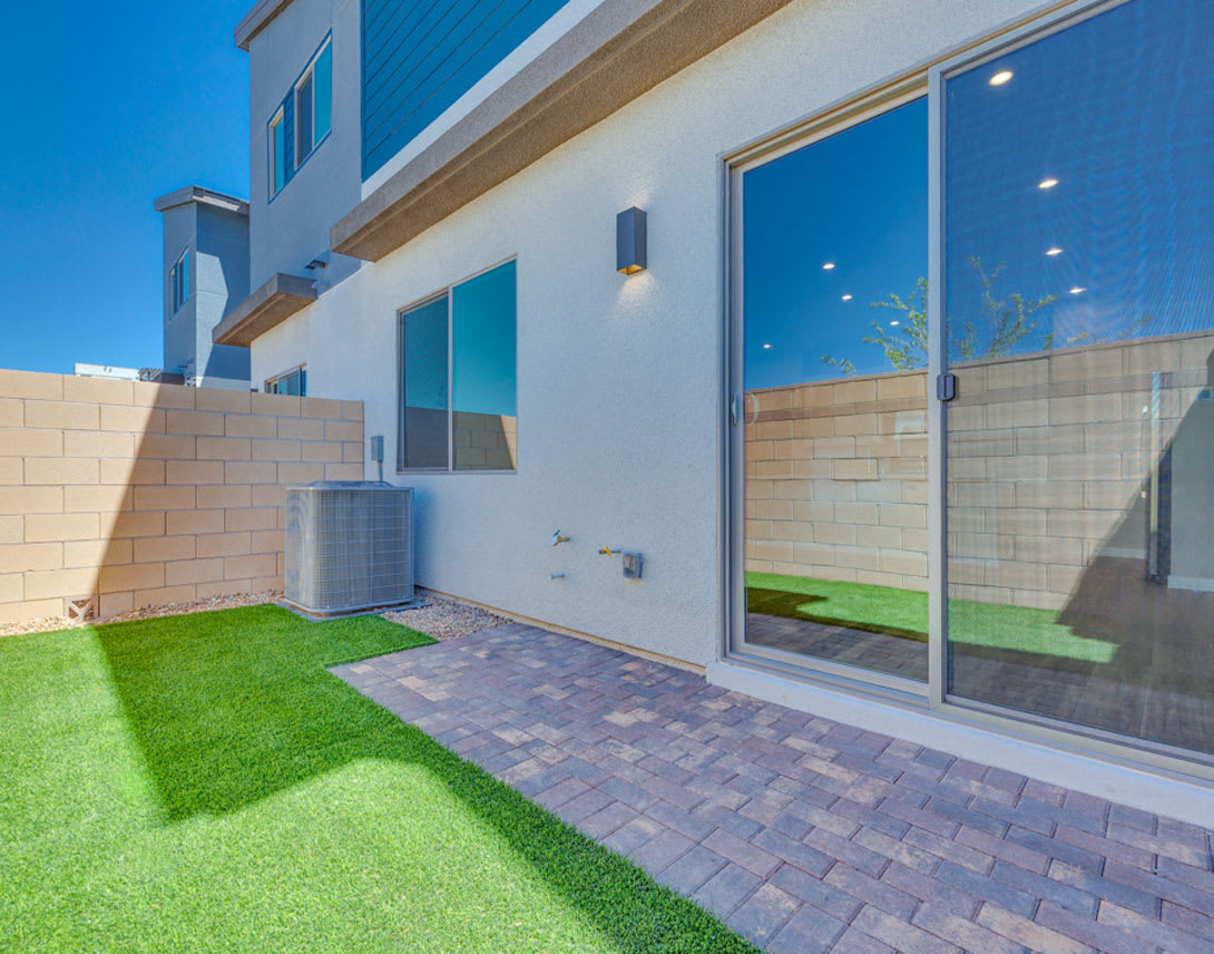 A modern, two-story building with a paved patio and a well-manicured lawn in the foreground, surrounded by a clear blue sky.