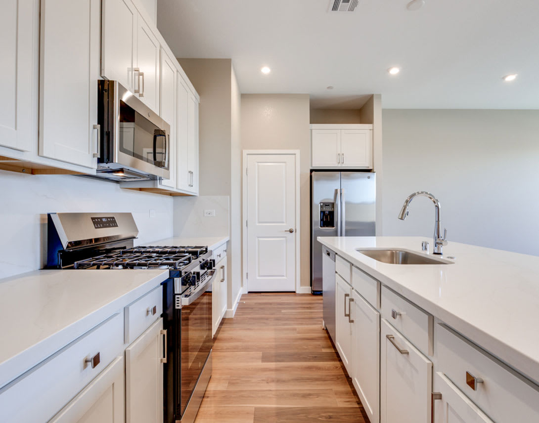 A modern, well-equipped kitchen with white cabinets, stainless steel appliances, and a wooden floor, creating a clean and spacious atmosphere.