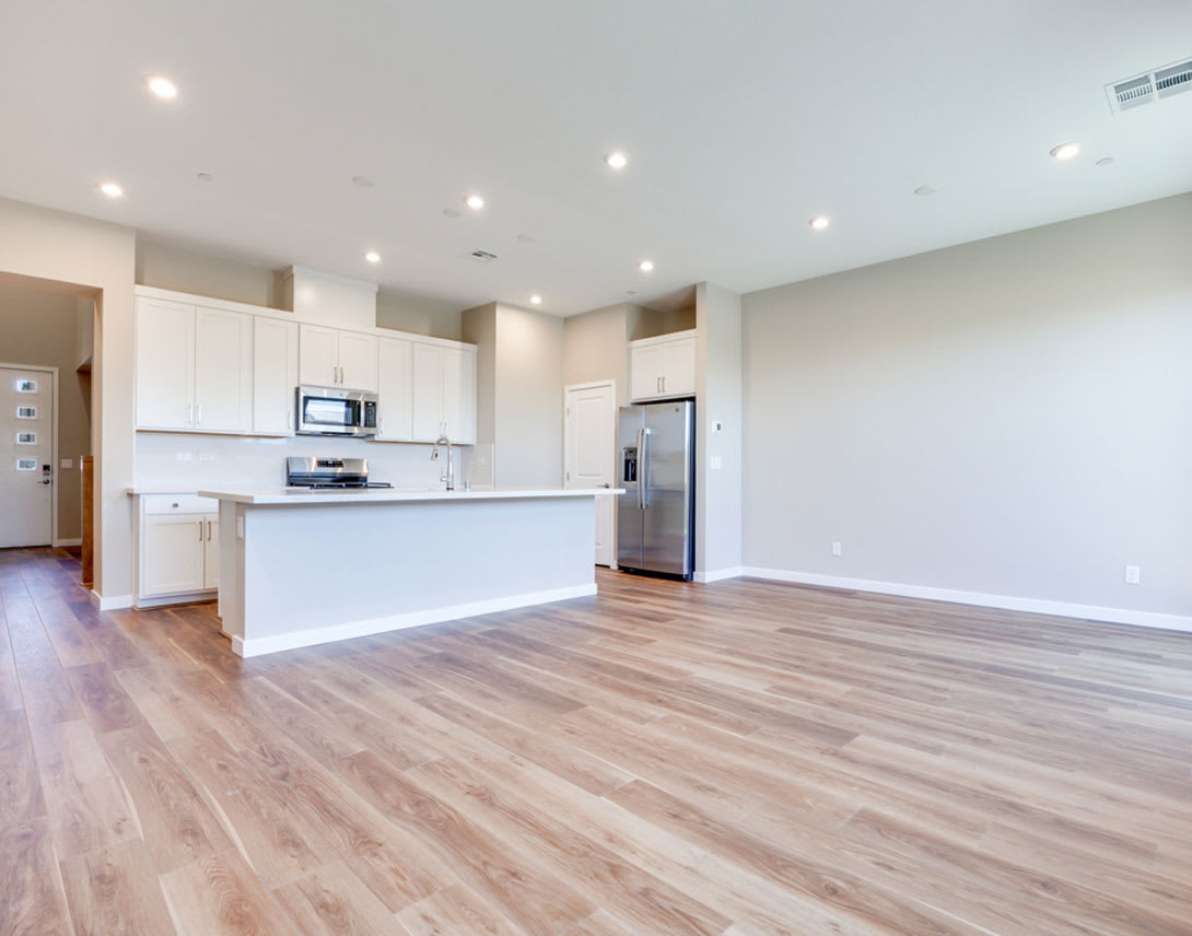 A spacious and modern kitchen with white cabinets, stainless steel appliances, and a hardwood floor that extends into an open living area.